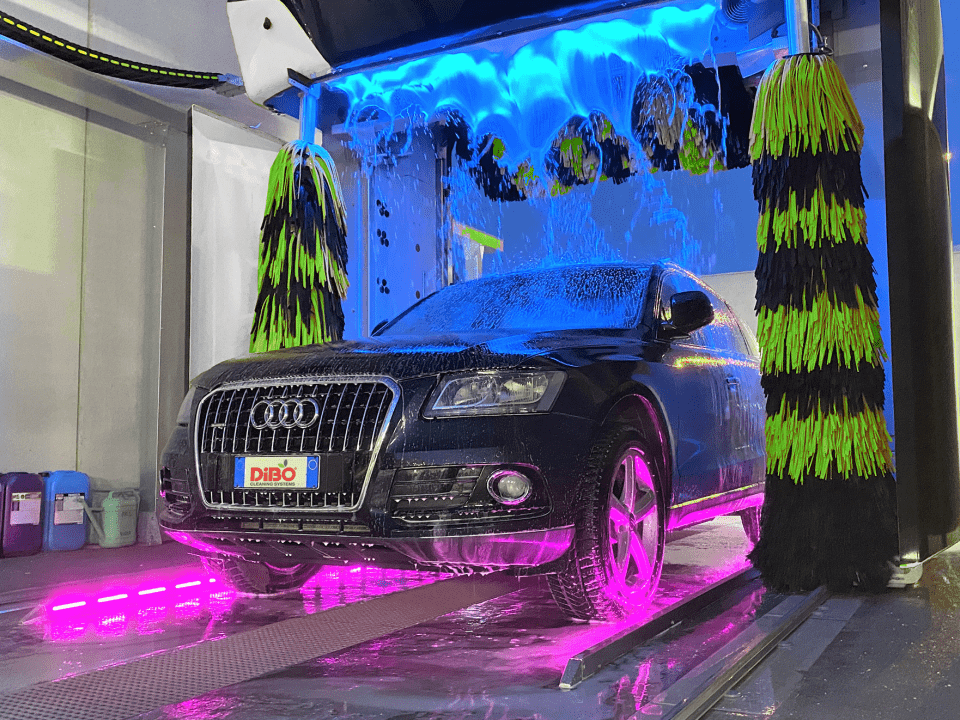 Blaues LED-beleuchtetes Wasser fällt in Zeitlupe auf das Auto, während die Räder und der Unterboden rosa beleuchtet werden - Disco Car Wash